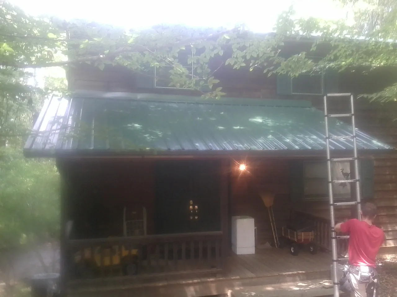 Worker on a ladder at the green porch roof of a wooded cabin in Lincoln